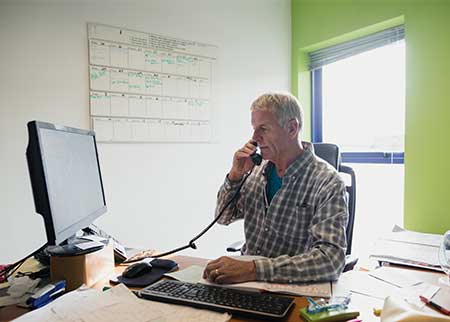 Office Owner Sitting at Desk on Phone with Workers Compensation Insurance in Concord, NC